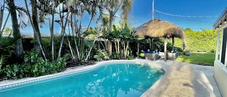 This beautiful Pompano Beach home has a heated pool and rustic tiki hut with outdoor lounging and dining, surrounded by lush landscaping. Enjoy hours of fun with family and friends.