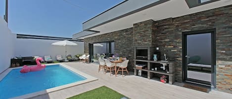 Pool area with dining table,  sun loungers, couch, sun umbrella, and grill area