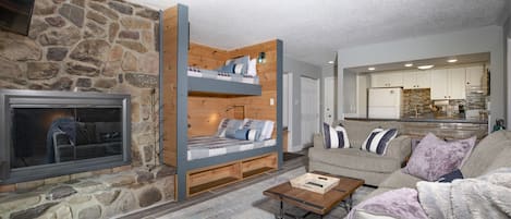 Living room w/ stone fireplace and built-in bunk beds w/ device chargers and reading lamps