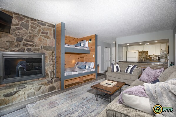 Living room w/ stone fireplace and built-in bunk beds w/ device chargers and reading lamps