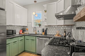 You will love cooking in this bright kitchen with green cabinets and modern appliances. The hexagonal tile backsplash and open shelving add a touch of elegance to the space.