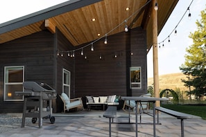 Back patio is decked out with cozy furniture, bbq, picnic table & string lights.