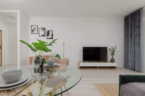 An open-plan living and dining area featuring a green sofa, a circular glass dining table, and light-toned furniture, creating a bright and airy feel.