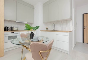 A kitchen with white cabinetry, wooden accents, and a round dining table paired with elegant green chairs, blending functionality with stylish design.