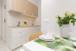 The functional kitchenette space has high-quality appliances. There is a white dining table next to it.