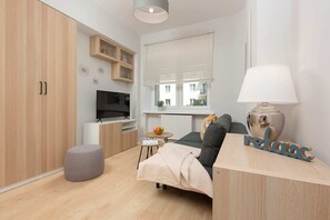 A cosy living room with a sofa and TV ensures that you can relax and unwind during your stay. The stylish kitchenette is visible in the background.