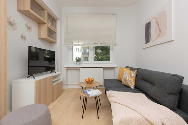 The living area has a comfortable green sofa next to which stands a coffee table. A flat-screen TV is visible opposite for evening entertainment.