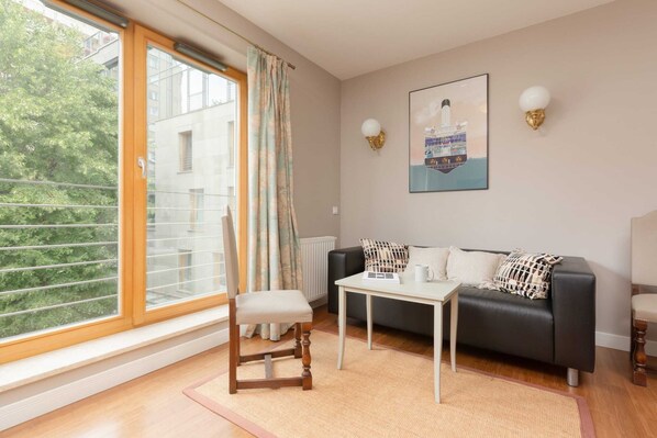 A cozy living room features a sofa, coffee table, and glass doors leading to a balcony, offering a view of greenery.
