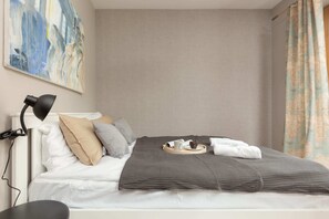 A bedroom includes a double bed with grey bedding and pillows, placed beside a large window with views of trees.