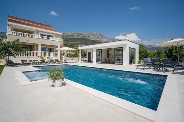 he spacious sun-deck area spreads on two levels, around the pool and a few steps below on the grassplot