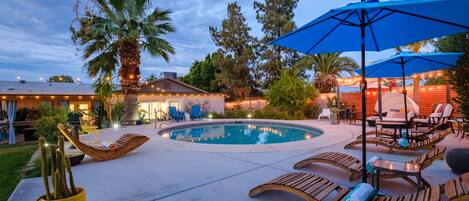 Stunning resort-style backyard with multiple lounge chairs, umbrellas, & cabanas