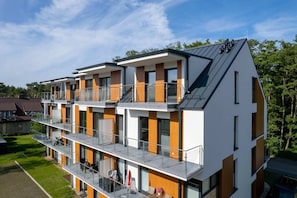 A modern apartment building with orange and white accents, large windows, and balconies.