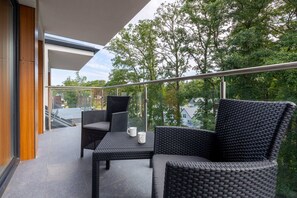 A well-furnished balcony with modern wicker chairs and a small table, surrounded by trees, offering a serene outdoor experience.