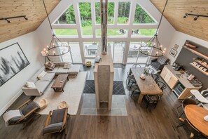 The stunning Great Room provides ample room for rest and relaxation. It features a large double-sided fireplace, dining table, games table, coffee bar, OLED TV, modern art, dramatic floor-to-ceiling windows and two exits to the back deck and lawn. 