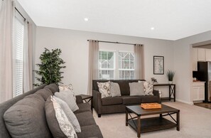 This spacious living room is perfect for entertaining or unwinding after a long day. Large windows fill the space with natural light, and modern décor, a comfy sofa, coffee table, and flat-screen TV create a bright, inviting spot for movie nights or 