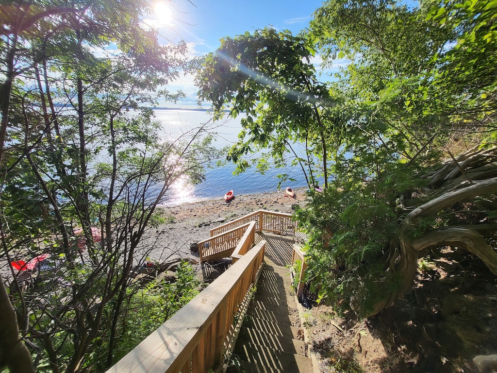A long set of stairs leads from a Lake Champlain vacation home down to a private beach with kayaks on a bright and sunny day.