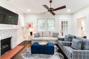 Living room space complete with sofa, coffee table, smart TV, fireplace, and ceiling fan.