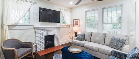 Living room space complete with sofa, coffee table, smart TV, fireplace, and ceiling fan.