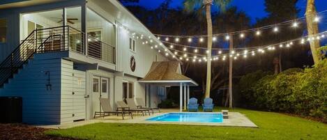 Night-time view of front yard with covered porch with the fabulous pool.