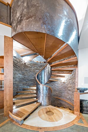 Striking spiral staircase with custom wood and metal design against stone walls.