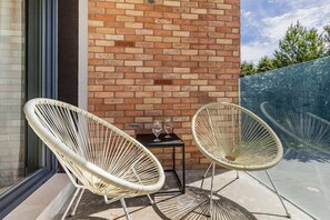 A balcony with wicker chairs and a view of a brick facade, perfect for enjoying a morning coffee or evening relaxation.
