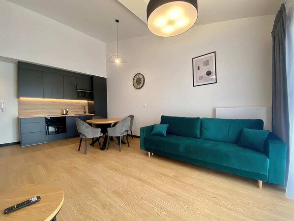 A stylish living area featuring a teal sofa, a round coffee table, and a dining space, blending comfort with modern design.
