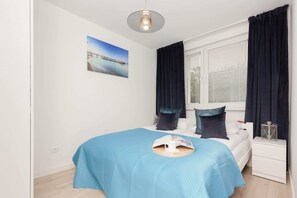 A bedroom with a double bed dressed in turquoise bedding, complemented by modern decor and soft lighting.
