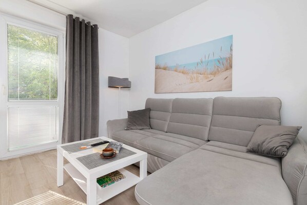 A cozy living room with a comfortable gray corner sofa, a coffee table, and modern decor, complemented by natural light from large windows.

