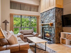 Living Room - Large couch and chaise, cozy real wood fireplace, 65" SmartTV with cable channels, sliding doors leading onto spacious patio.