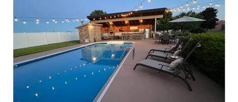 Large heated pool with outdoor lights and lounge chairs. 