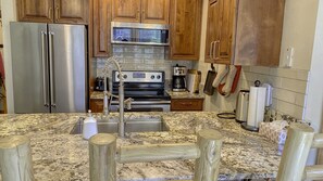 Fully equipped kitchen. Granite countertop, rustic wood cabinets, four stools.  