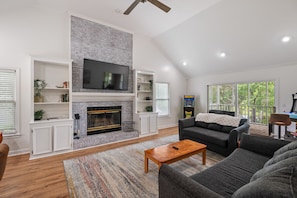 The living area has seating for the entire family and includes a wet bar with a mini fridge, two arcade machines, and a chess table.