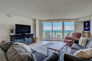 A cozy living room with big windows and a door leading to the balcony, filling the space with light and ocean views.