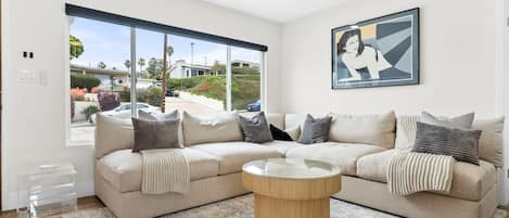 Living room is wide open with a large, custom sectional and original artwork. 