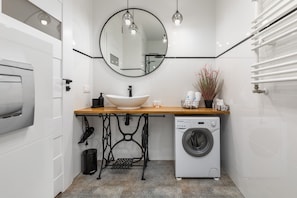 A modern bathroom with a round mirror, stylish sink, and a washing machine for guest convenience.
