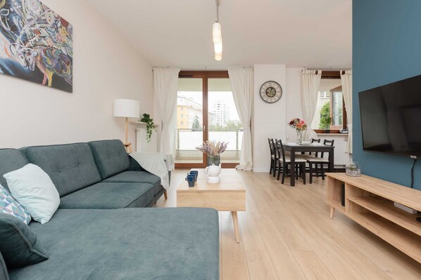 A spacious living room featuring a teal sofa, wooden coffee table, and a TV mounted on a blue accent wall, creating a modern and cozy atmosphere.
