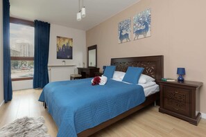 A bright bedroom with a double bed dressed in blue bedding, wooden nightstands, and tasteful artwork on the walls.
