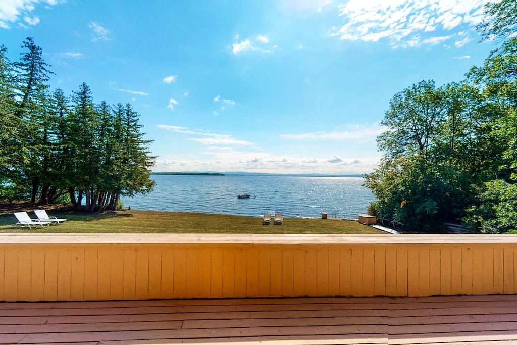 A summer scene of a Lake Champlain vacation home from the deck on a sunny day with trees surrounding the lawn