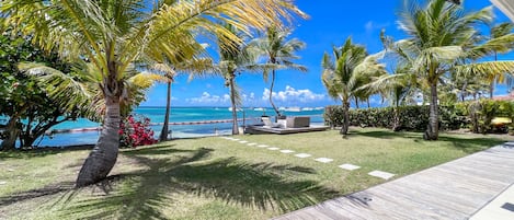 Breathtaking view of the garden, the sea and the lagoon of Saint-François from the terrace of the villa with coconut palms and bougainvillea.
