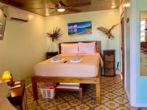 Queen bed area with side chair, AC, TV, side tables and small dresser