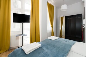 A different perspective of the bedroom, highlighting the large windows with yellow curtains and a TV for entertainment.
