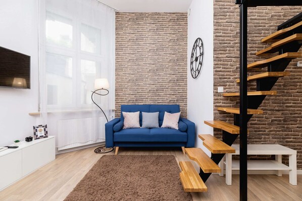 A cozy living room featuring a plush sofa and a simple coffee table. A large window allows natural light to fill the space.