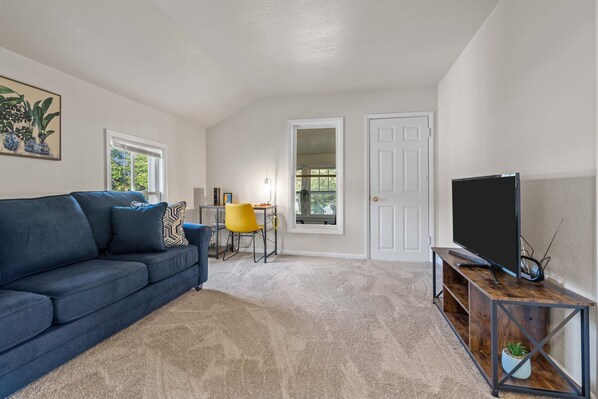 Living area from view of the kitchen. Includes smart TV, queen size sleeper sofa and desk with an office chair.