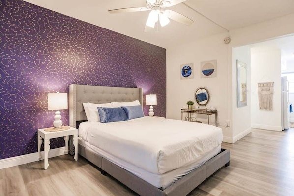 Unwind in the Comfort of a Queen Size Bed, Enhanced by Elegant Wallpaper, Soft Lamp Illumination, and a Gentle Ceiling Fan for a Tranquil Atmosphere.