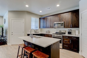 The gourmet kitchen features an island with seating for three and is equipped with stainless steel appliances, including a microwave, gas stove, and spacious refrigerator.