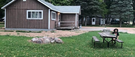 Exterior view from behind cabin showcases the picnic table and firepit