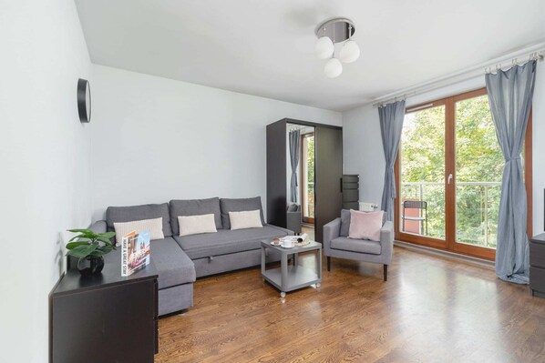 Spacious living room with a sofa, armchair, and coffee table, with large windows and curtains allowing natural light.