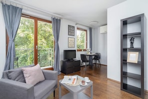 Another view of the living room, featuring a modern shelving unit and a desk near a large window.