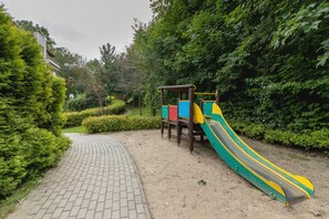  Outdoor playground with a slide and a pathway, surrounded by bushes and trees.