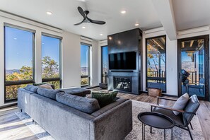 Floor to ceiling windows in the bright living room, with big TV and fireplace